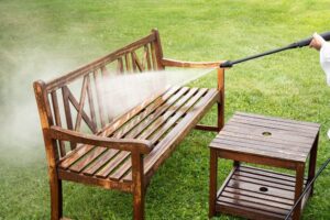 Pressure Washing. Outdoor Furniture. Close up view of person working cleaning pressure washing wooden garden furniture bench outdoors in summer. 