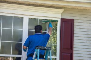 Window Cleaning. A Caucasian man on a ladder wearing blue latex gloves and listening to ear buds washing a window with a squeegee.