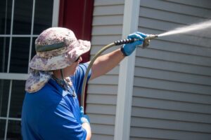 Why Vancouver Residents Trust Us for Pressure Washing Services. A Caucasian man with a latex gloves holding water sprayer wand pressure washing a house.