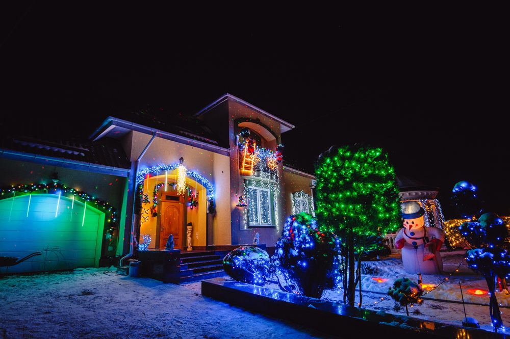 Christmas Light Installation. House Adorned with Christmas Holiday Lights and Decorations including Santa Snowman and Giant Trees Illuminated at Night. Christmas Lights outside on a House.