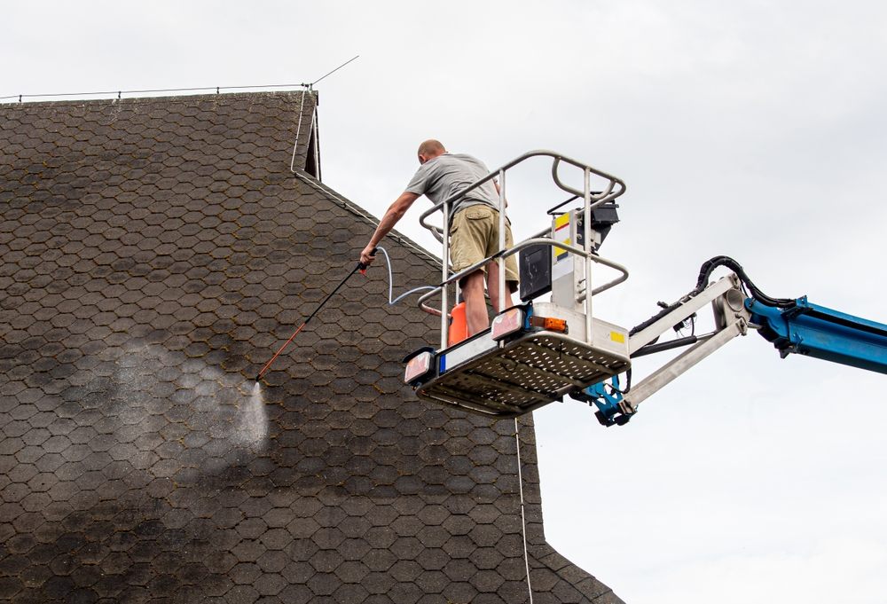 The Safest and Most Effective Method for Roof Moss Removal. Man a homeowner spraying moss removing chemical to a domestic home roof in summer outdoors. Moss removal concept.